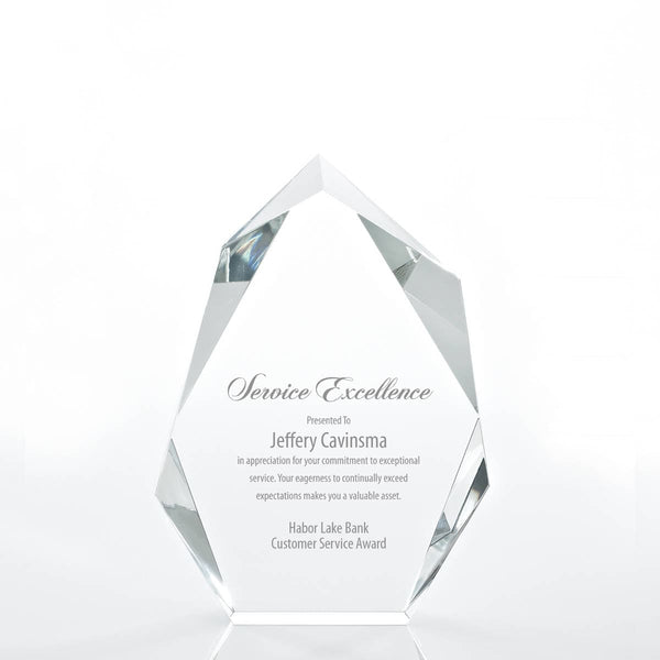 Clear crystal award shaped like a peak with angled facets catching light, laser-engraved text visible in the center