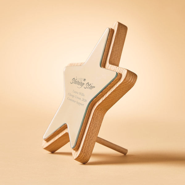 A star-shaped wooden desk plaque with a white center panel and natural wood edges, standing on a small wooden support leg against a warm beige background. The panel is printed with the text 'Shining Star' and customer support details.