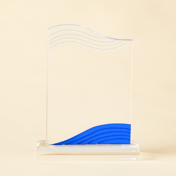 A clear acrylic award trophy plaque with a blue wave design at the bottom, standing on a clear acrylic base against a warm beige background.