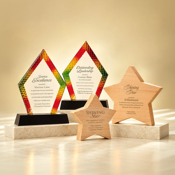 Four personalized corporate award plaques displayed on a light beige marble surface against a warm beige background. The set includes two diamond-shaped acrylic plaques with a colorful gradient pattern (red, orange, yellow, green) and two wooden star plaques in light natural wood.